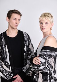 Black and gray patterned cardigans with ribbed cuffs, worn over black and gray tops. The fabric has a textured, woven appearance.