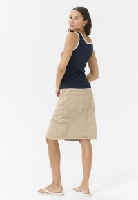 Débardeur marine avec bord blanc, associé à une jupe beige mi-longue comportant plusieurs poches et une finition texturée. Des sandales simples.