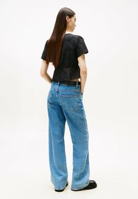 Zwarte, kortekorte top met een gestructureerd patroon; gecombineerd met lichtblauwe, wijde jeans en zwarte plateau schoenen. Achteraanzicht.
