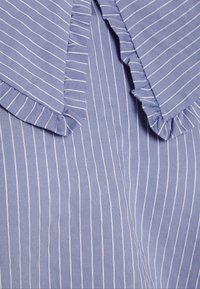 Gros plan sur un tissu bleu clair avec de fines rayures verticales blanches et des bords de col froncés sur un vêtement.