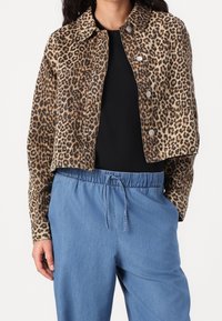 Denimjack met luipaardprint en een cropped ontwerp, voorzien van zilveren knopen, een kraag en een gestructureerde stof. Gecombineerd met lichtblauwe broek met trekkoord.