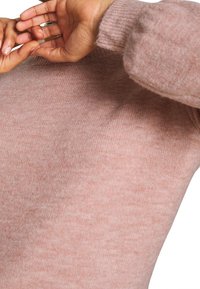 Jasnoróżowy sweter wykonany z miękkiej, teksturowanej tkaniny z prążkowanymi mankietami i okrągłym dekoltem, prezentujący subtelny, jednolity wzór kolorystyczny.