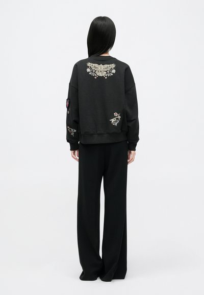 Must mustriga, millel on selja ja varrukatel kantud lille- ja linnukujundused; koos vabama musta pükstega. Pehme kangas, mugav lõige.