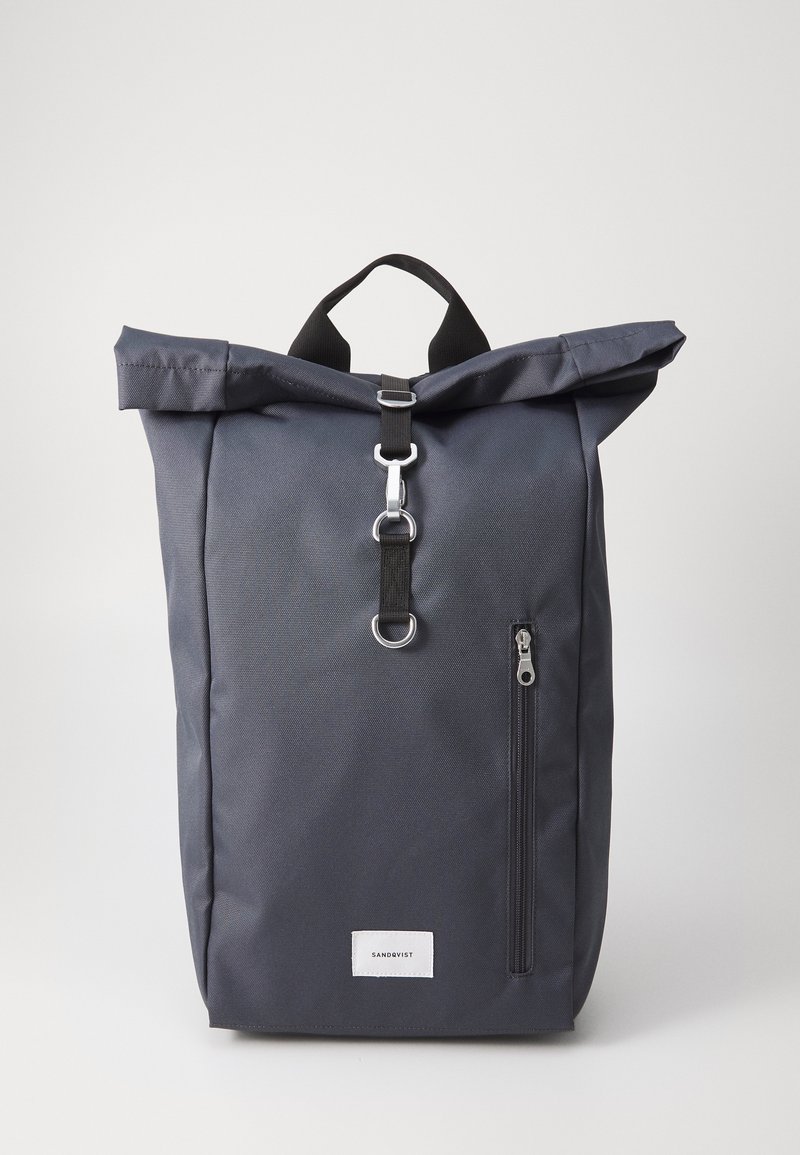 Zaino grigio a scomparsa realizzato in tessuto resistente, dotato di una tasca con zip, accessori in metallo e una maniglia superiore per un facile trasporto.
