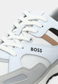 Zapatillas blancas y azul claro con detalles en gris. Cuentan con materiales de malla y sintéticos, cordones redondos y un logo lateral que dice "BOSS".