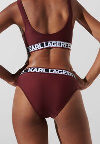 Kastanjas kr�āsas bikini tops un bottoms ar melnu un baltu zīmola jostasvīru. Izgatavots no gludas materiāla ar ciešu piegulšanu un minimālām šuvēm.