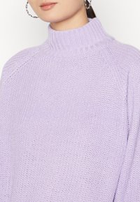 Pull en tricot lavande clair avec un col haut, doté d'une coupe ample et de détails côtelés le long de l'encolure et des poignets.