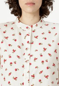 White fabric shirt featuring a small floral print of pink roses and green leaves, button-down front with round collar and textured stripes.
