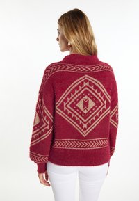 Pulover bordeaux cu o textură pufoasă, decorat cu modele geometrice aurii și un guler înalt, conceput cu mâneci largi și o croială lejeră.