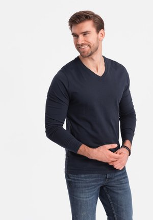 Marineblå langærmet V-hals skjorte lavet af bomuldsblanding, med en glat tekstur og en slim fit, parret med lyseblå jeans.