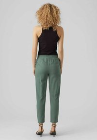 Groene lichtgewicht broeken met een elastische tailleband, tapered pijpenontwerp en enkellange pasvorm. Gecombineerd met zwarte hakschoenen.
