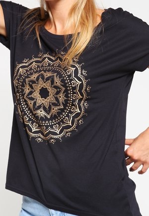Camiseta negra con un diseño de mandala dorado en el centro. Hecha de tela suave, con un corte relajado y un escote amplio.