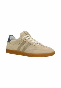 Baskets en daim beige avec lacets blancs, deux bandes latérales, patch de talon bleu et semelle en caoutchouc marron, vues sous un angle trois quarts.