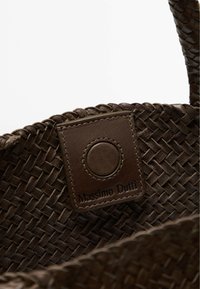 Tkaná hnědá kabelka s texturovaným povrchem, obsahující hnědou koženou visačku s embosovaným nápisem "Massimo Dutti" a kulatým detailem.
