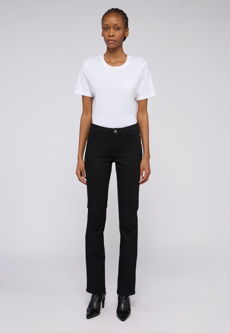 Černé denimové džíny se rovnými nohavicemi, ve spojení s bílým bavlněným tričkem. Model má na sobě černé boty na vysokém podpatku. Jednoduchý design, bez vzorů.