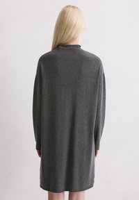 Abito grigio lavorato a maglia con collo a imboccare, maniche lunghe, vestibilità rilassata e un orlo che si ferma sopra il ginocchio. Caratterizzato da una texture morbida e un design minimal.