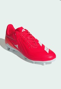 Botín de fútbol sintético rojo con acentos blancos, que presenta un diseño elegante y aerodinámico, una parte superior texturizada y seis tacos blancos de agarre en la suela.
