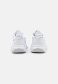 Paire de baskets blanches Reebok vues de dos, avec une semelle épaisse et le logo Reebok visible sur la languette du talon.