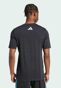Sort bomulds-T-shirt med korte ærmer, prydet med et hvidt Adidas-logo på den øverste del af ryggen. Pasformen er standard, designet til afslappet brug.