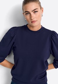 Temno modra majica z napihnjenimi kratkimi rokavi, okroglim izrezom in gladko teksturo. Ima prilagojen pas in minimalne šivne detajle.