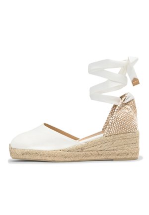 Espadrille blanche en toile avec talon compensé en jute tressé et ruban à nouer autour de la cheville sur fond blanc.