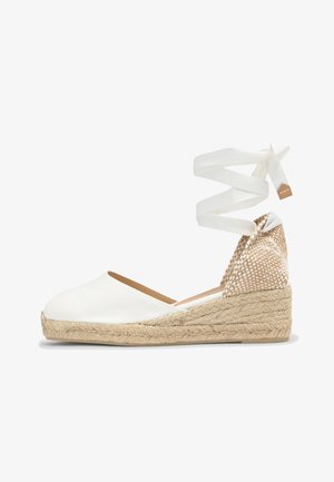 White canvas espadrille with braided jute wedge heel and ankle wrap ribbon against white background.