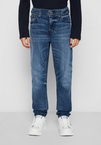 Jeans in denim blu scuro con taglio dritto, design a cinque tasche e chiusura con bottone. Indossati con sneakers bianche.