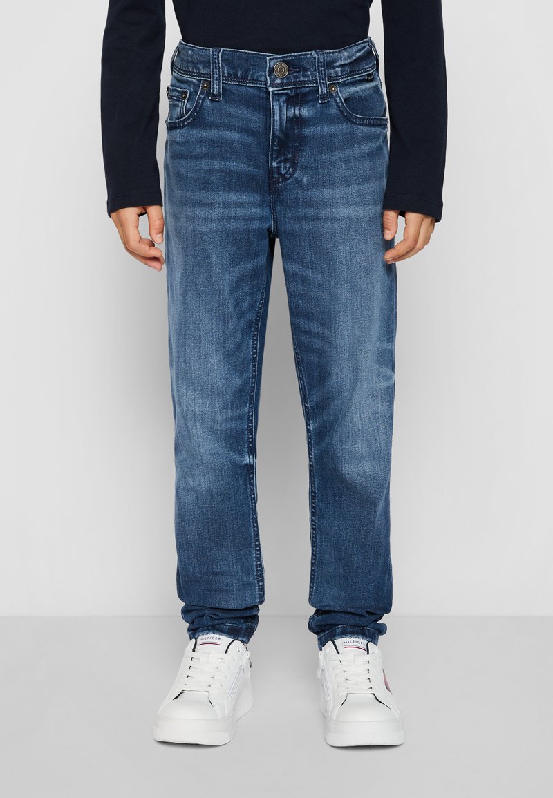Jeans in denim blu scuro con taglio dritto, design a cinque tasche e chiusura con bottone. Indossati con sneakers bianche.