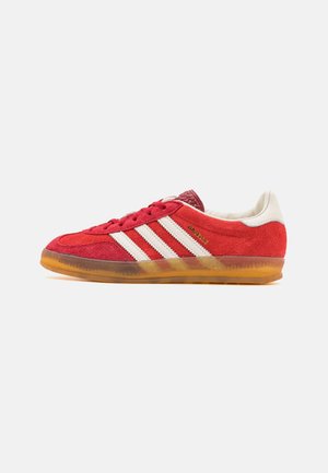 Rød ruskinds Adidas Gazelle sneaker med hvide striber, hvid hælkappe, røde snørebånd og gennemsigtig gummisål.