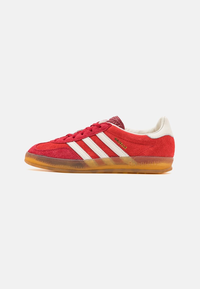 Baskets Adidas Gazelle en daim rouge avec des bandes blanches, languette blanche au talon, lacets rouges et semelle en gomme translucide.