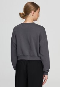 Przycięta szara bluza z gładką fakturą, prążkowanym dekoltem i szerokimi rękawami, w połączeniu z czarnymi luźnymi spodniami.