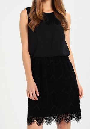Czarna sukienka z gładkim, bezrękawowym topem oraz koronkową spódnicą z falowanym brzegiem, tworząca efekt teksturowanej warstwowości.