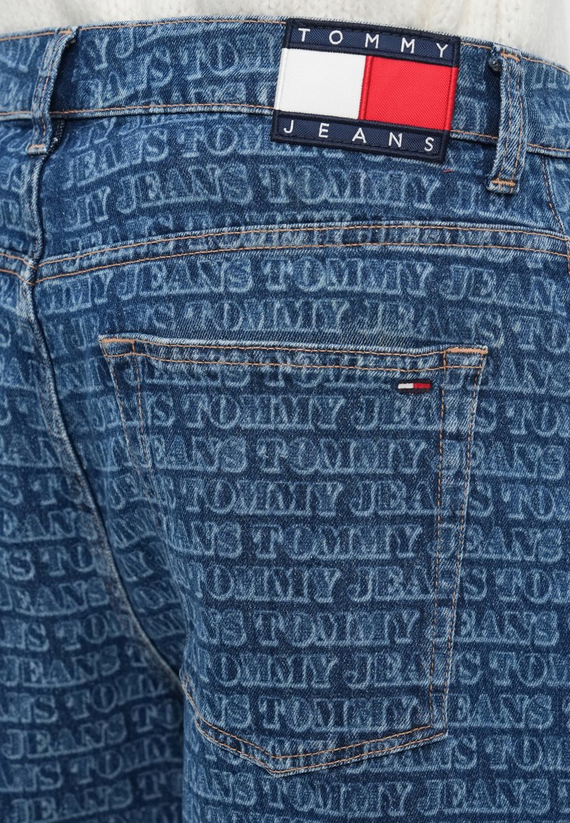 Vaqueros de mezclilla con un estampado tonal del logo "TOMMY JEANS". Tejido azul con costuras naranjas, etiqueta de parche en la cinturilla que muestra los colores de la marca.