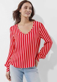 Rot-weißer gestreifter Blusen mit V-Ausschnitt und langen Ärmeln, aus einem glatten Stoff gefertigt; passt gut zu hellblauen Jeans.