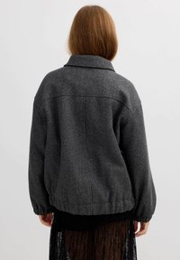 Chaqueta de mezcla de lana gris con cuello, hombros caídos y puños elásticos; presenta un ajuste relajado y detalles de costura.