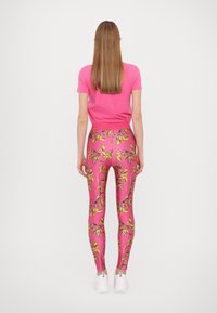 T-shirt rosa abbinato a leggings rosa con un motivo floreale giallo e nero, e sneakers bianche. Vista da dietro.