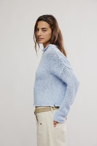 Ανοιχτό μπλε πλεκτό πουλόβερ με ριμπ λαιμόκοψη και σχεδιασμό με ραμμένες ώμους. Φορεμένο πάνω από μπεζ παντελόνια, παρουσιάζοντας υφασμάτινη υφή.