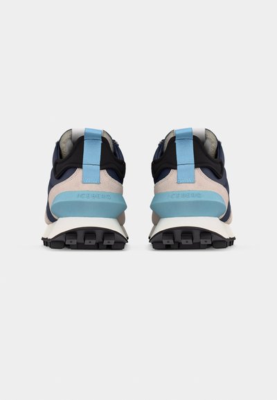 Paire de baskets bleu marine, beige et bleu clair avec semelles noires et languettes bleu clair vues de dos sur un fond blanc.