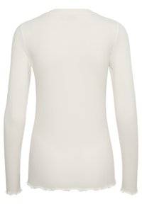 Haut à manches longues côtel�é de couleur crème, avec un col arrondi et des bords festonnés, fabriqué en tissu doux et extensible.