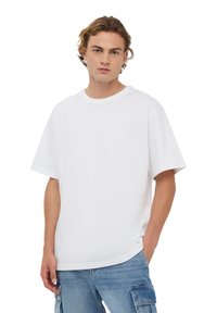 T-shirt bianca a maniche corte in cotone, con scollo rotondo e vestibilità comoda. Abbinata a pantaloni cargo blu.