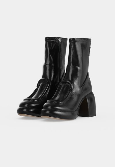 Paire de bottes mi-mollet en cuir noir brillant avec talons blocs épais et fermetures éclair latérales, avec un grand panneau décoratif matelassé à l'avant.