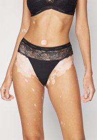 Schwarze Calvin Klein Spitzenunterwäsche mit Blumenspitze am Bund, glattem Stoff und geschwungenem Schnitt an den Beinen.