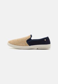 Chaussures à enfiler avec une tige en beige tissé, des accents en textile bleu marine et une semelle en caoutchouc blanc, comportant un petit logo de marque doré près du talon.