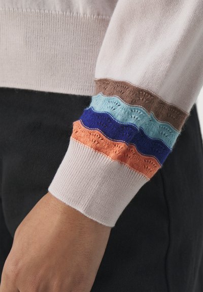 Manche de pull en tricot présentant une base rose clair avec des rayures texturées et en dents de scie de couleur marron, bleu clair, bleu marine, orange et crème.