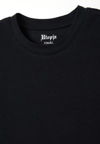 T-shirt in cotone nero con scollo rotondo, caratterizzato dal nome del marchio "Utopia" stampato in bianco con carattere gotico sull'etichetta interna, taglia XS.