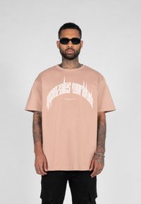 Lyserød oversized t-shirt med hvid grafisk tekst, korte ærmer, rund hals og en blød bomuldsstruktur, parret med sorte cargo shorts.