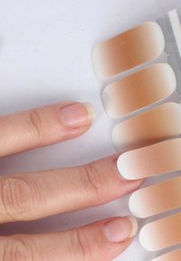 Nagellackstreifen in einem Farbverlauf von Beige bis hellbraun, die neben einer Hand mit natürlichen, unlackierten Nägeln angeordnet sind.
