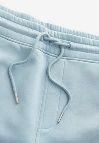 Pantaloni sweat blu chiaro con vita regolabile tramite cordoncino con punte in metallo argentato, texture morbida e dettagli con tasche laterali.