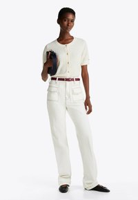 Cardigan bianco lavorato a maglia con maniche corte e bottoni, abbinato a pantaloni a gamba larga color crema a vita alta, valorizzati da una cintura bordeaux e ballerine nere.