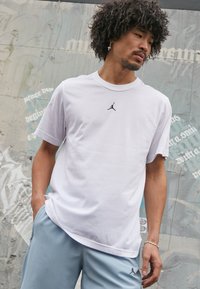 Hvid bomulds T-shirt med korte ærmer, der har et sort Jordan-logo på brystet. Kombination med lyseblå sportsshorts.